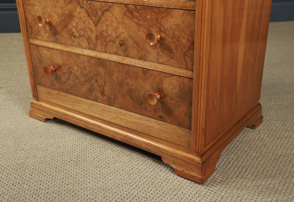 An Art Deco chest of drawers in figured burr walnut featuring six graduated drawers with turned wooden handles and carved shoulder details. View IX