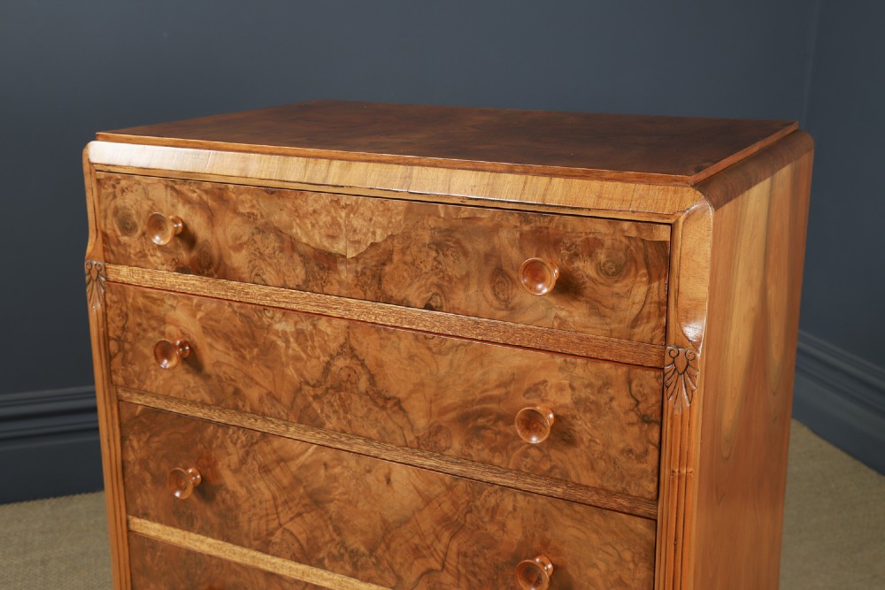 An Art Deco chest of drawers in figured burr walnut featuring six graduated drawers with turned wooden handles and carved shoulder details. View X