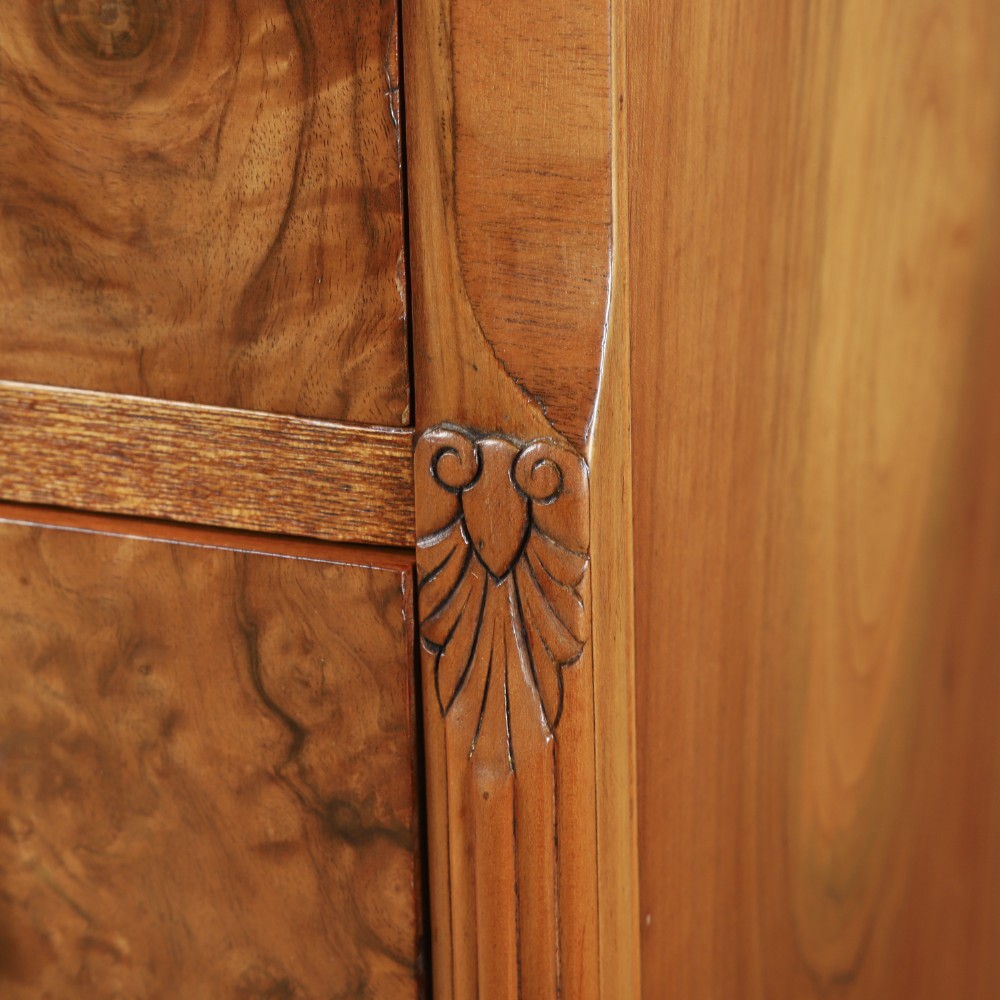 An Art Deco chest of drawers in figured burr walnut featuring six graduated drawers with turned wooden handles and carved shoulder details. View XII