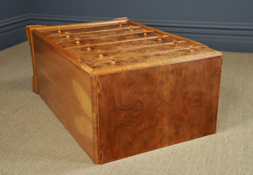 An Art Deco chest of drawers in figured burr walnut featuring six graduated drawers with turned wooden handles and carved shoulder details. View XV