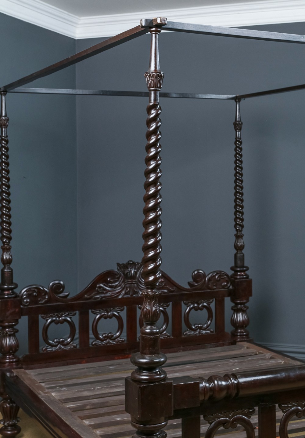 An antique dark timber king-size four-poster bed featuring spiral turned posts, a carved footboard with circular cut-out details, and an upper canopy frame. View V