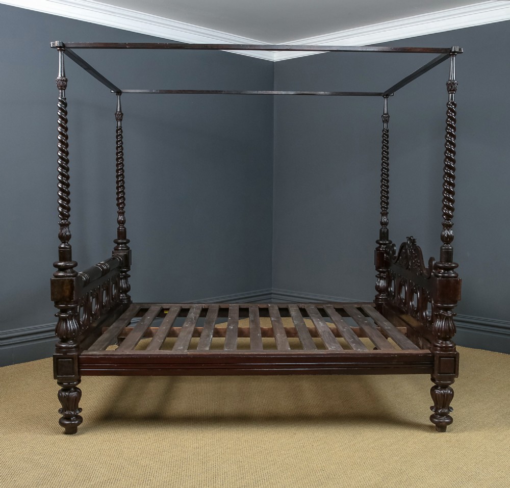 An antique dark timber king-size four-poster bed featuring spiral turned posts, a carved footboard with circular cut-out details, and an upper canopy frame. View X