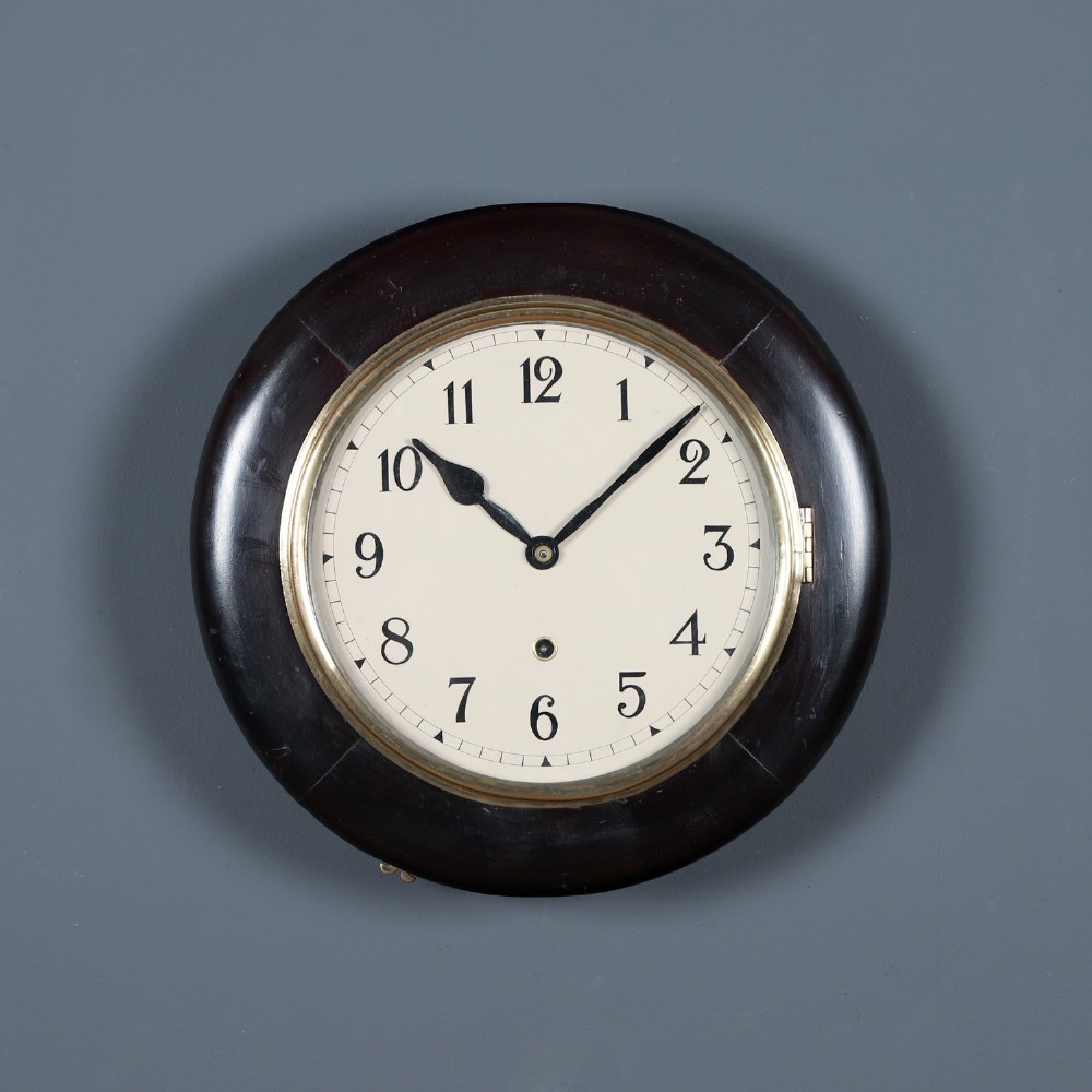 A circular antique dark mahogany wall clock featuring a white dial with black Arabic numerals and a brass bezel.