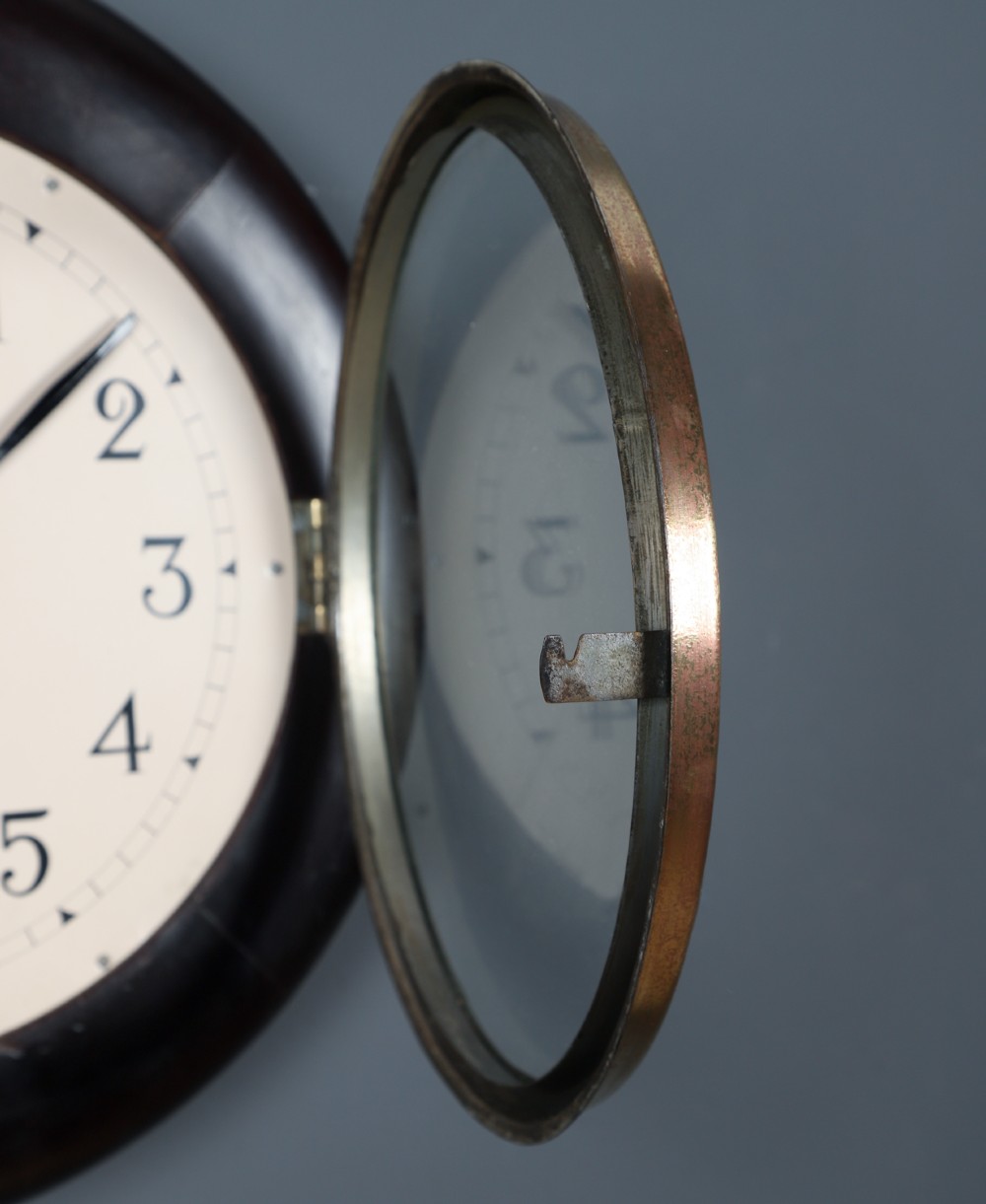 A circular antique dark mahogany wall clock featuring a white dial with black Arabic numerals and a brass bezel. View III