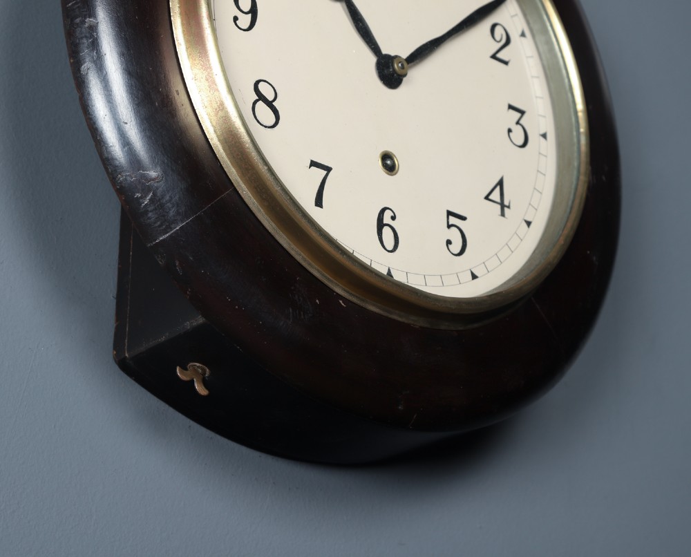 A circular antique dark mahogany wall clock featuring a white dial with black Arabic numerals and a brass bezel. View VI