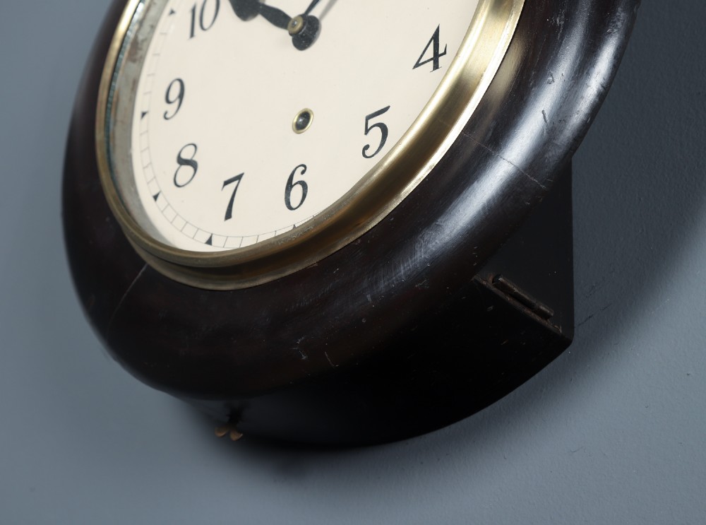 A circular antique dark mahogany wall clock featuring a white dial with black Arabic numerals and a brass bezel. View VII