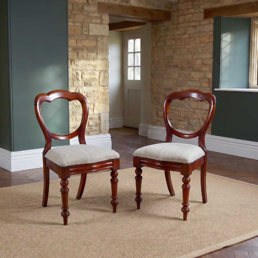 A pair of mid-nineteenth century Victorian mahogany dining chairs featuring balloon back frames, turned front legs, and neutral fabric upholstered seats.