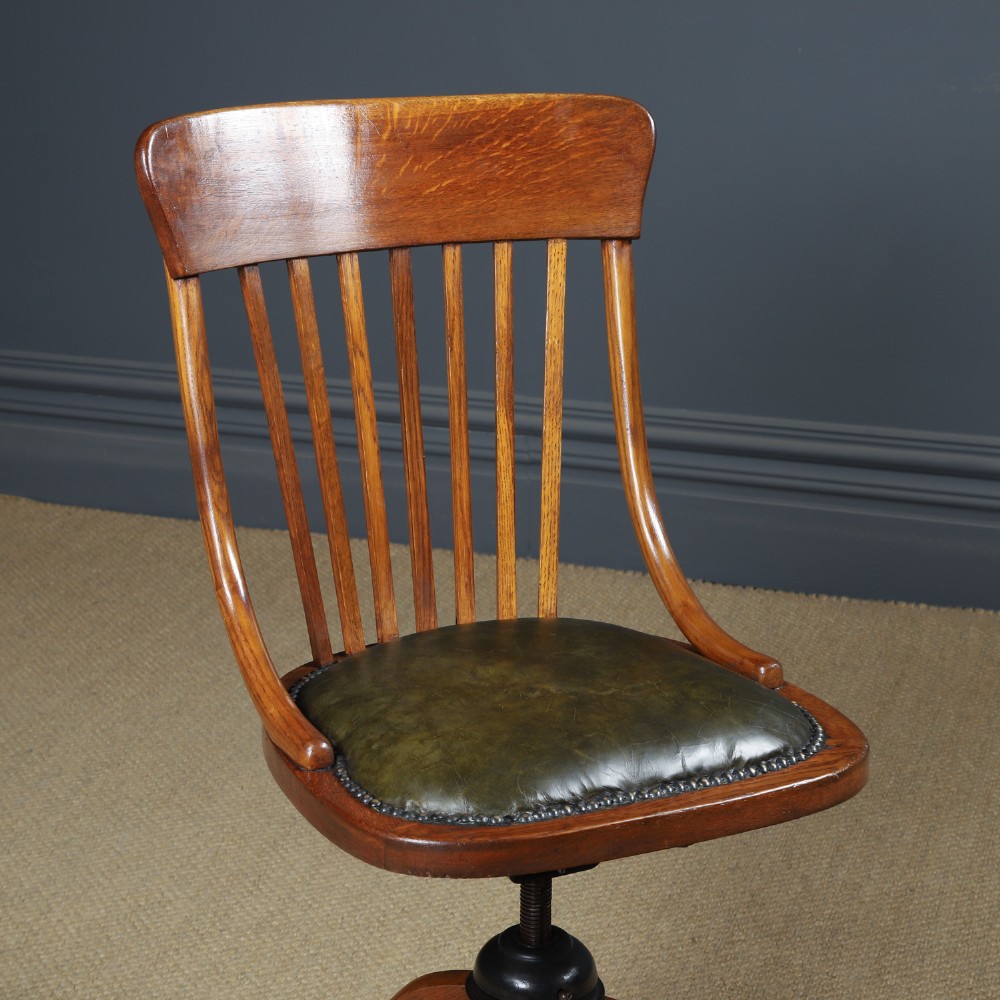 A George V period golden oak revolving desk chair featuring a curved spindle backrest, quadruped base, and a padded green leather seat secured with brass studs. View II