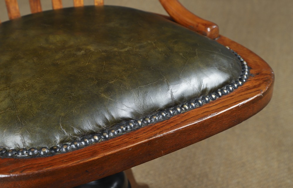 A George V period golden oak revolving desk chair featuring a curved spindle backrest, quadruped base, and a padded green leather seat secured with brass studs. View V