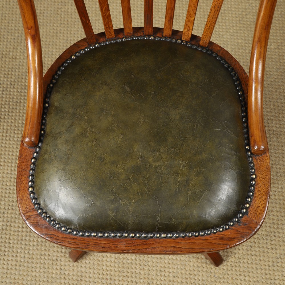 A George V period golden oak revolving desk chair featuring a curved spindle backrest, quadruped base, and a padded green leather seat secured with brass studs. View VI