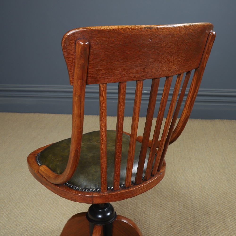 A George V period golden oak revolving desk chair featuring a curved spindle backrest, quadruped base, and a padded green leather seat secured with brass studs. View X