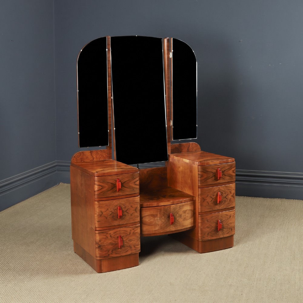 An Art Deco figured walnut dressing table featuring twin pedestal drawers, a central curved drawer, red handles, and a three-panel upright mirror.