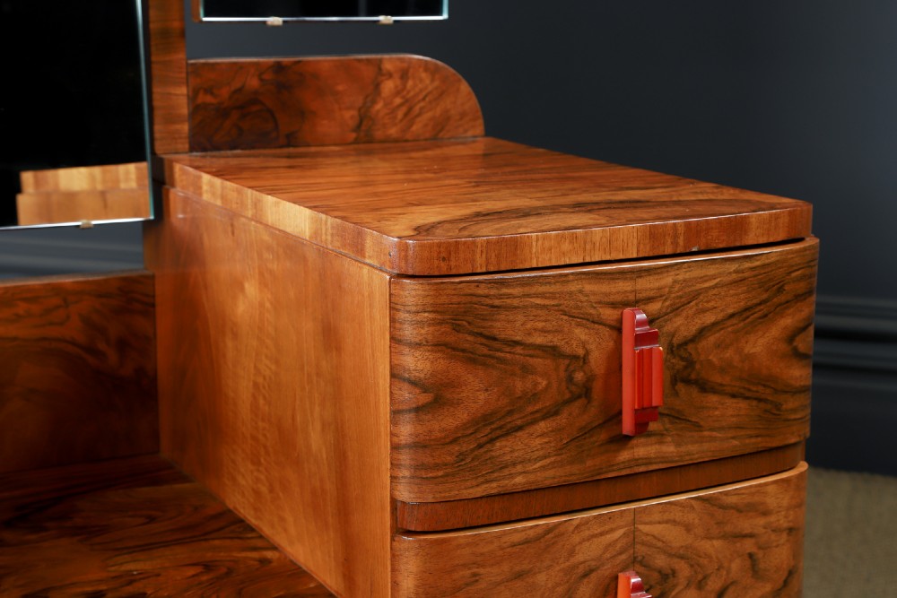 An Art Deco figured walnut dressing table featuring twin pedestal drawers, a central curved drawer, red handles, and a three-panel upright mirror. View VI
