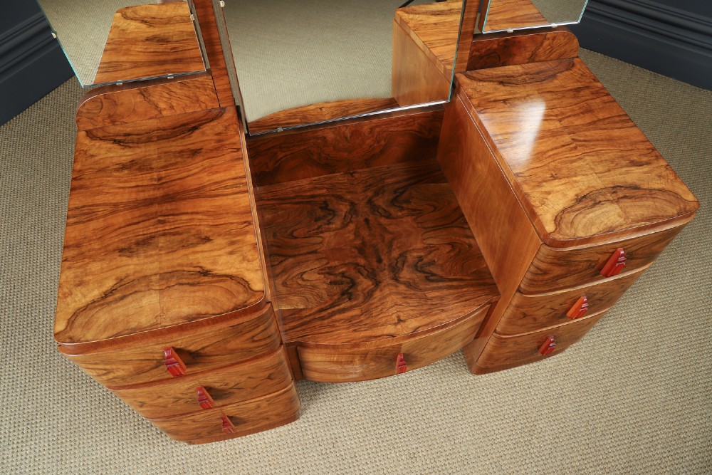 An Art Deco figured walnut dressing table featuring twin pedestal drawers, a central curved drawer, red handles, and a three-panel upright mirror. View VII