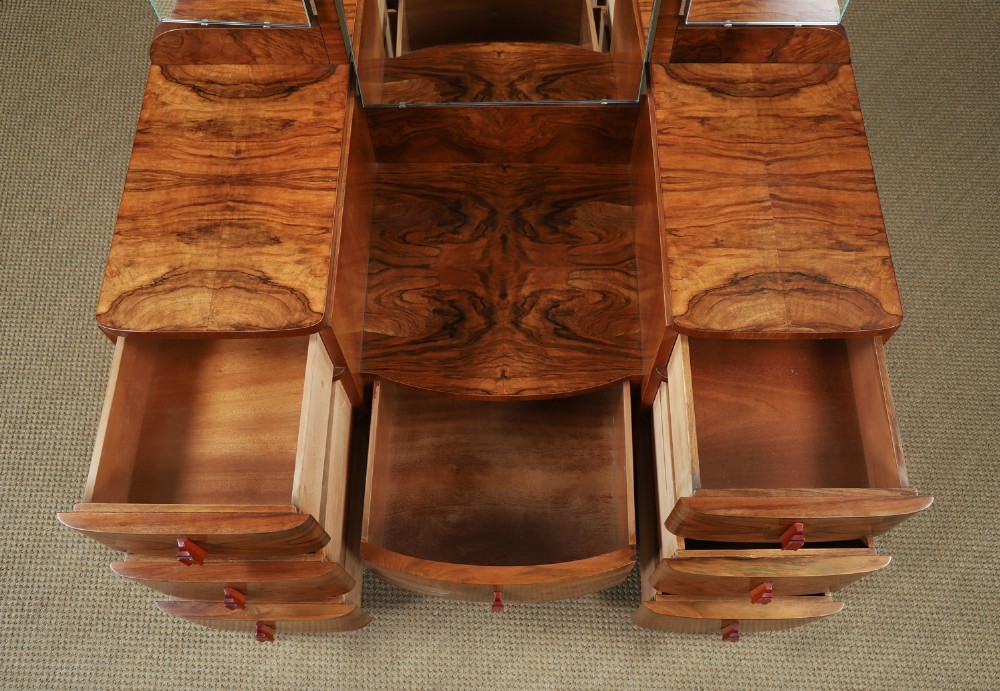 An Art Deco figured walnut dressing table featuring twin pedestal drawers, a central curved drawer, red handles, and a three-panel upright mirror. View X