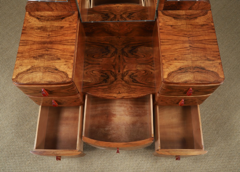 An Art Deco figured walnut dressing table featuring twin pedestal drawers, a central curved drawer, red handles, and a three-panel upright mirror. View XI