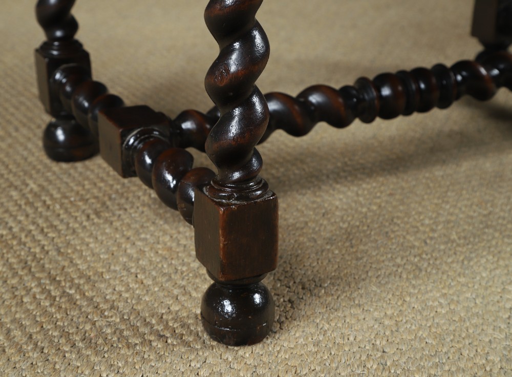 An antique 17th-century style dark oak armchair featuring deep-buttoned green leather upholstery, brass stud trim, and barley-twist turned legs and stretchers. View V