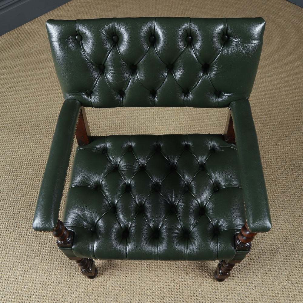 An antique 17th-century style dark oak armchair featuring deep-buttoned green leather upholstery, brass stud trim, and barley-twist turned legs and stretchers. View VIII