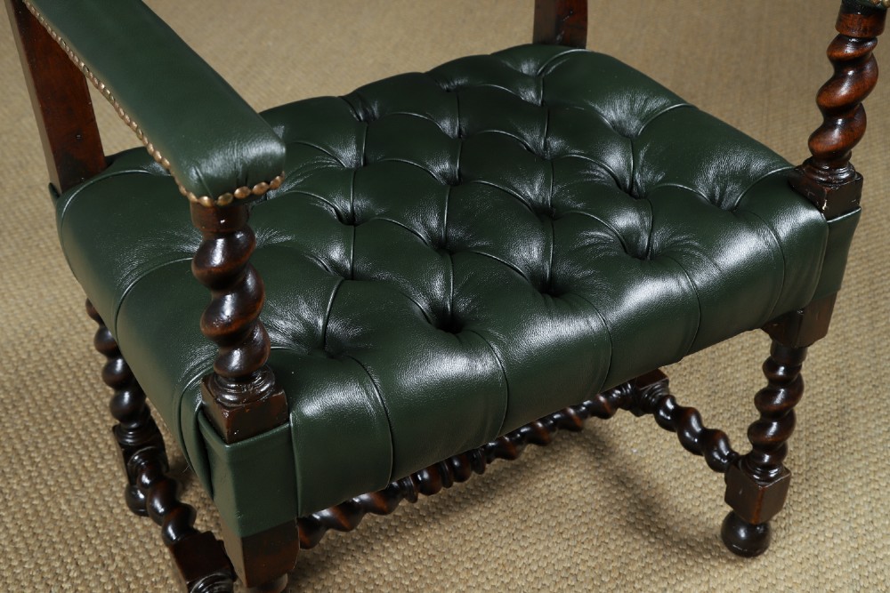 An antique 17th-century style dark oak armchair featuring deep-buttoned green leather upholstery, brass stud trim, and barley-twist turned legs and stretchers. View IX