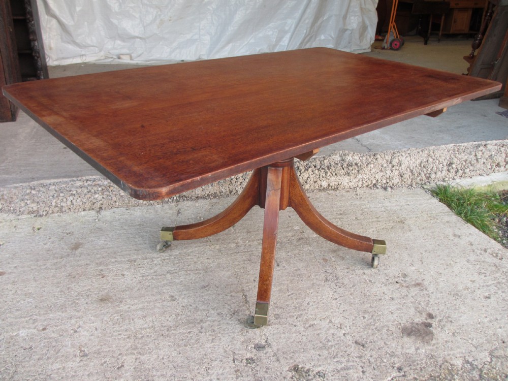 A 19th-century mahogany rectangular tilt-top dining table supported by a turned central pedestal with four splayed legs fitted with brass castors.