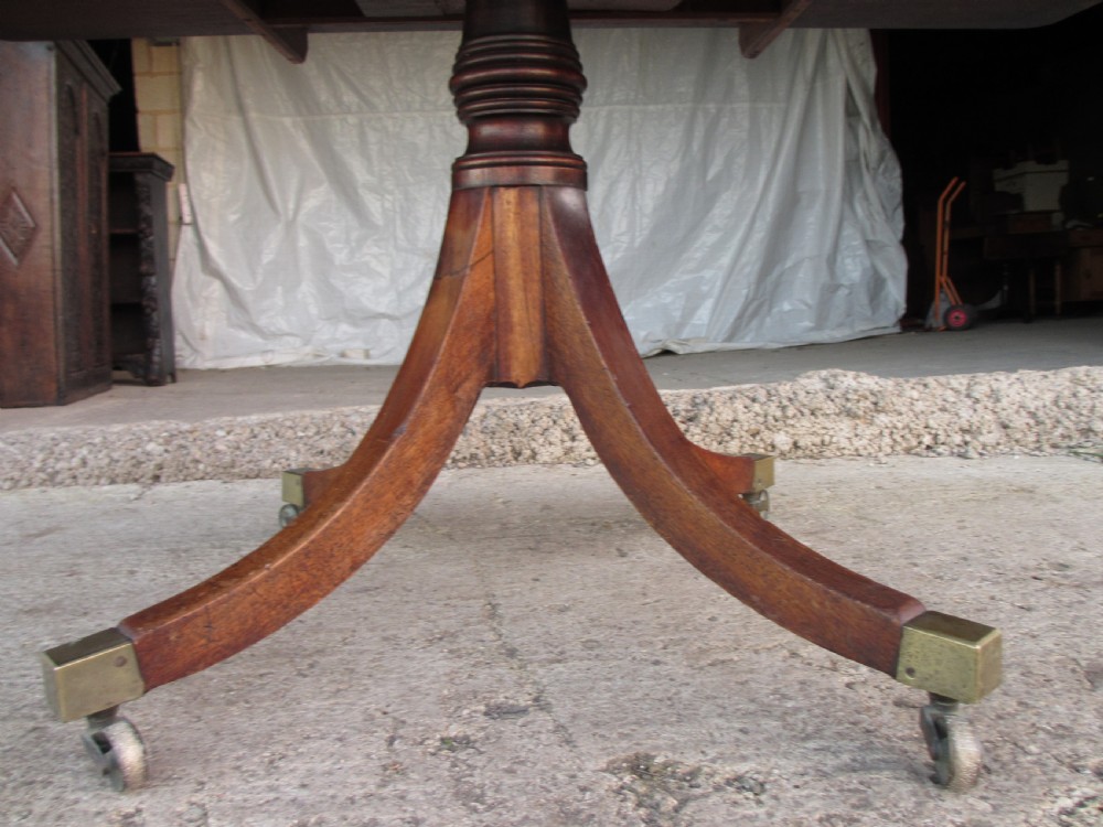 A 19th-century mahogany rectangular tilt-top dining table supported by a turned central pedestal with four splayed legs fitted with brass castors. View III
