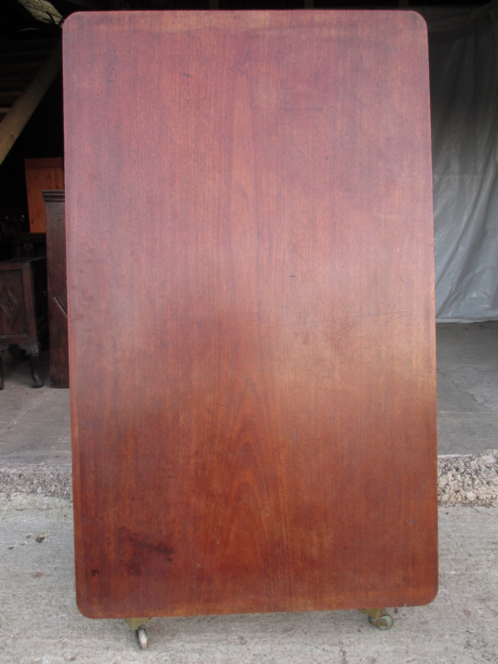 A 19th-century mahogany rectangular tilt-top dining table supported by a turned central pedestal with four splayed legs fitted with brass castors. View VI