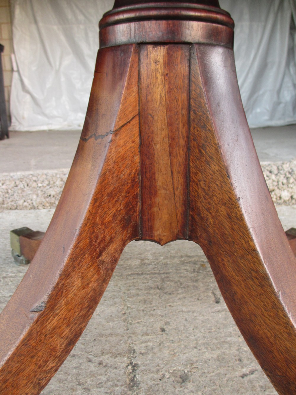 A 19th-century mahogany rectangular tilt-top dining table supported by a turned central pedestal with four splayed legs fitted with brass castors. View VII