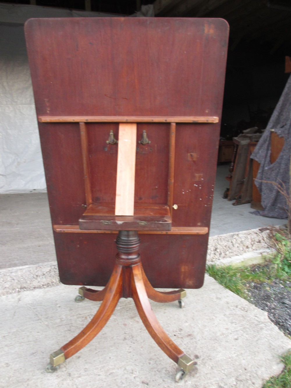 A 19th-century mahogany rectangular tilt-top dining table supported by a turned central pedestal with four splayed legs fitted with brass castors. View VIII
