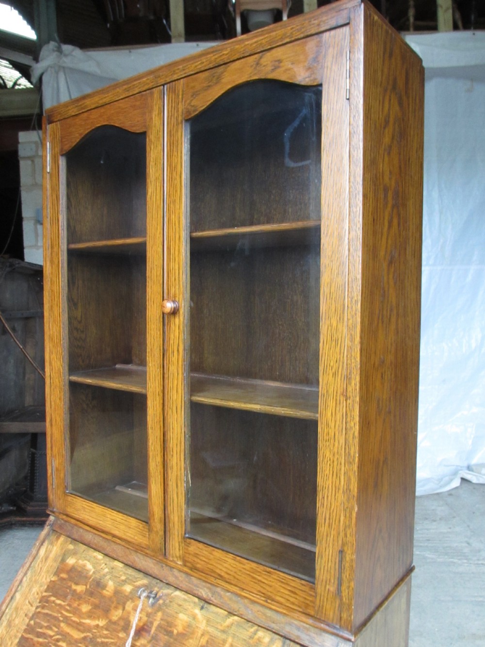 A narrow Edwardian oak bureau bookcase with twin glazed doors on the upper section above a fall-front writing desk and three drawers with wooden bun handles. View III