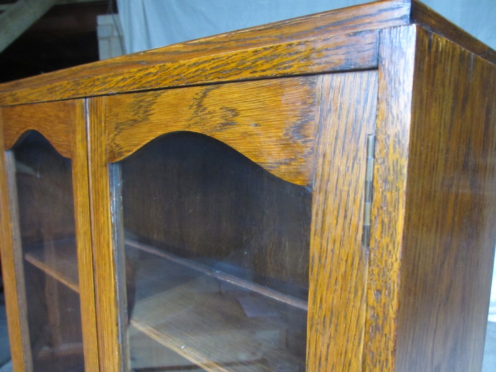 A narrow Edwardian oak bureau bookcase with twin glazed doors on the upper section above a fall-front writing desk and three drawers with wooden bun handles. View V