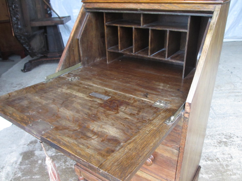 A narrow Edwardian oak bureau bookcase with twin glazed doors on the upper section above a fall-front writing desk and three drawers with wooden bun handles. View VII