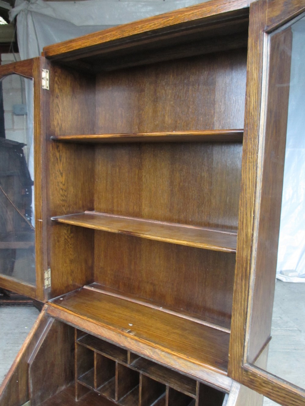 A narrow Edwardian oak bureau bookcase with twin glazed doors on the upper section above a fall-front writing desk and three drawers with wooden bun handles. View IX