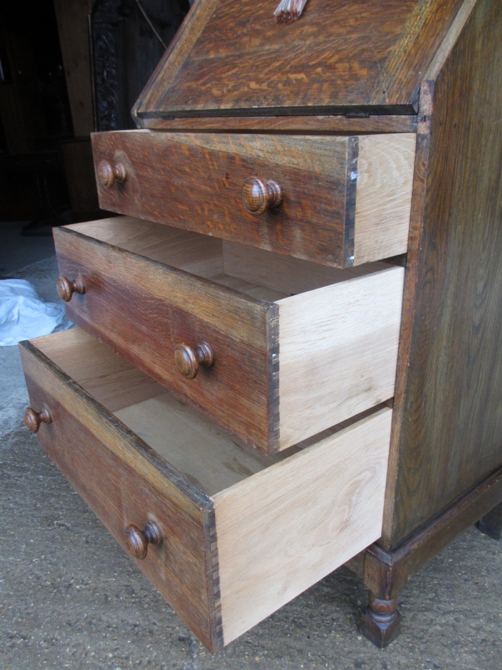 A narrow Edwardian oak bureau bookcase with twin glazed doors on the upper section above a fall-front writing desk and three drawers with wooden bun handles. View X
