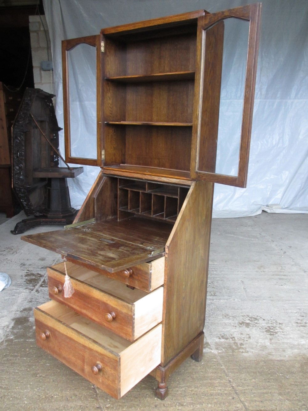 A narrow Edwardian oak bureau bookcase with twin glazed doors on the upper section above a fall-front writing desk and three drawers with wooden bun handles. View XI