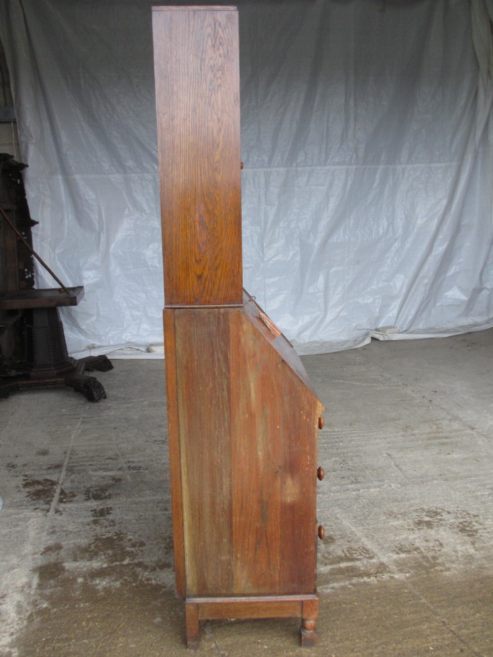 A narrow Edwardian oak bureau bookcase with twin glazed doors on the upper section above a fall-front writing desk and three drawers with wooden bun handles. View XIV