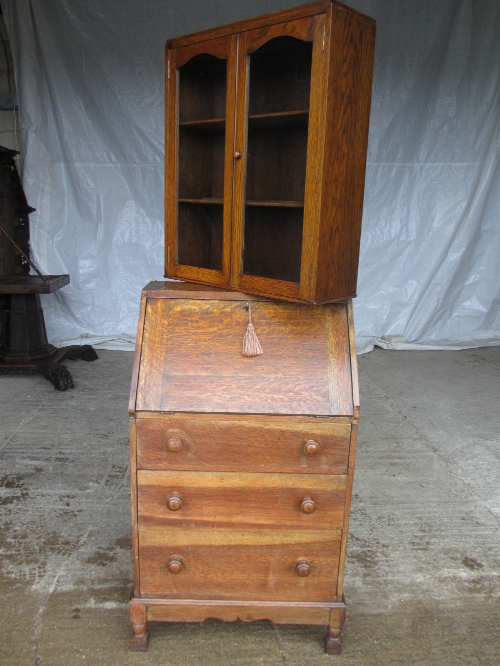 A narrow Edwardian oak bureau bookcase with twin glazed doors on the upper section above a fall-front writing desk and three drawers with wooden bun handles. View XVI