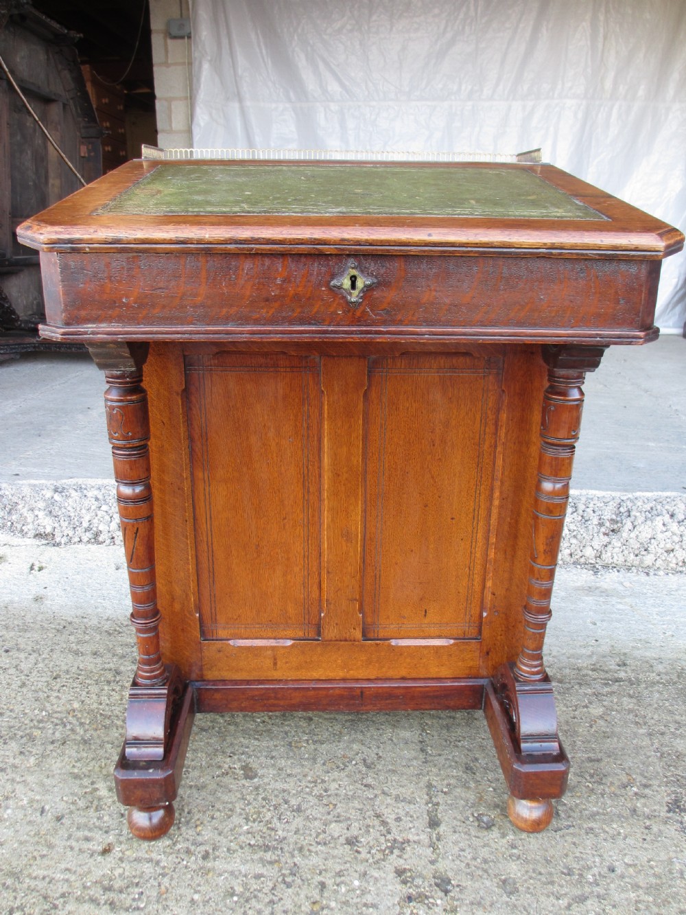 A Victorian oak davenport desk featuring a green leather writing surface, brass gallery rail, and turned front columns.