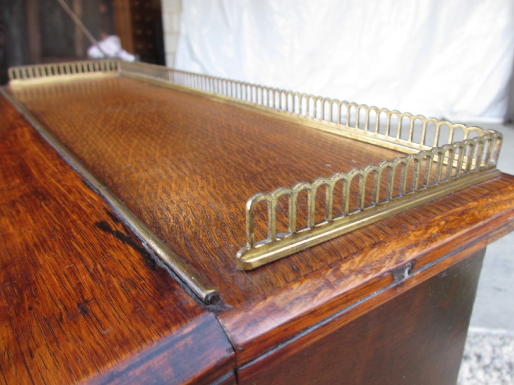 A Victorian oak davenport desk featuring a green leather writing surface, brass gallery rail, and turned front columns. View V