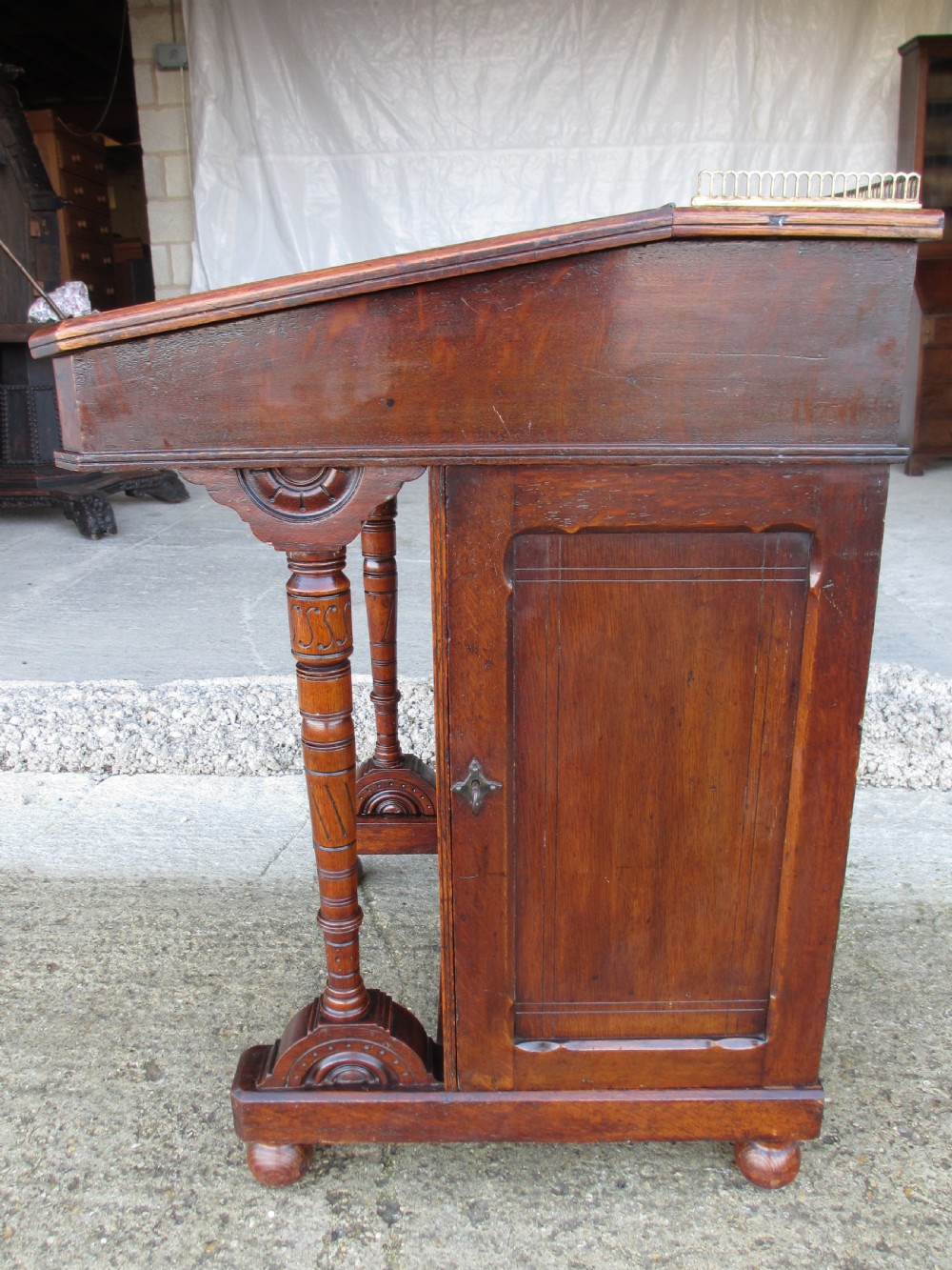 A Victorian oak davenport desk featuring a green leather writing surface, brass gallery rail, and turned front columns. View XIX