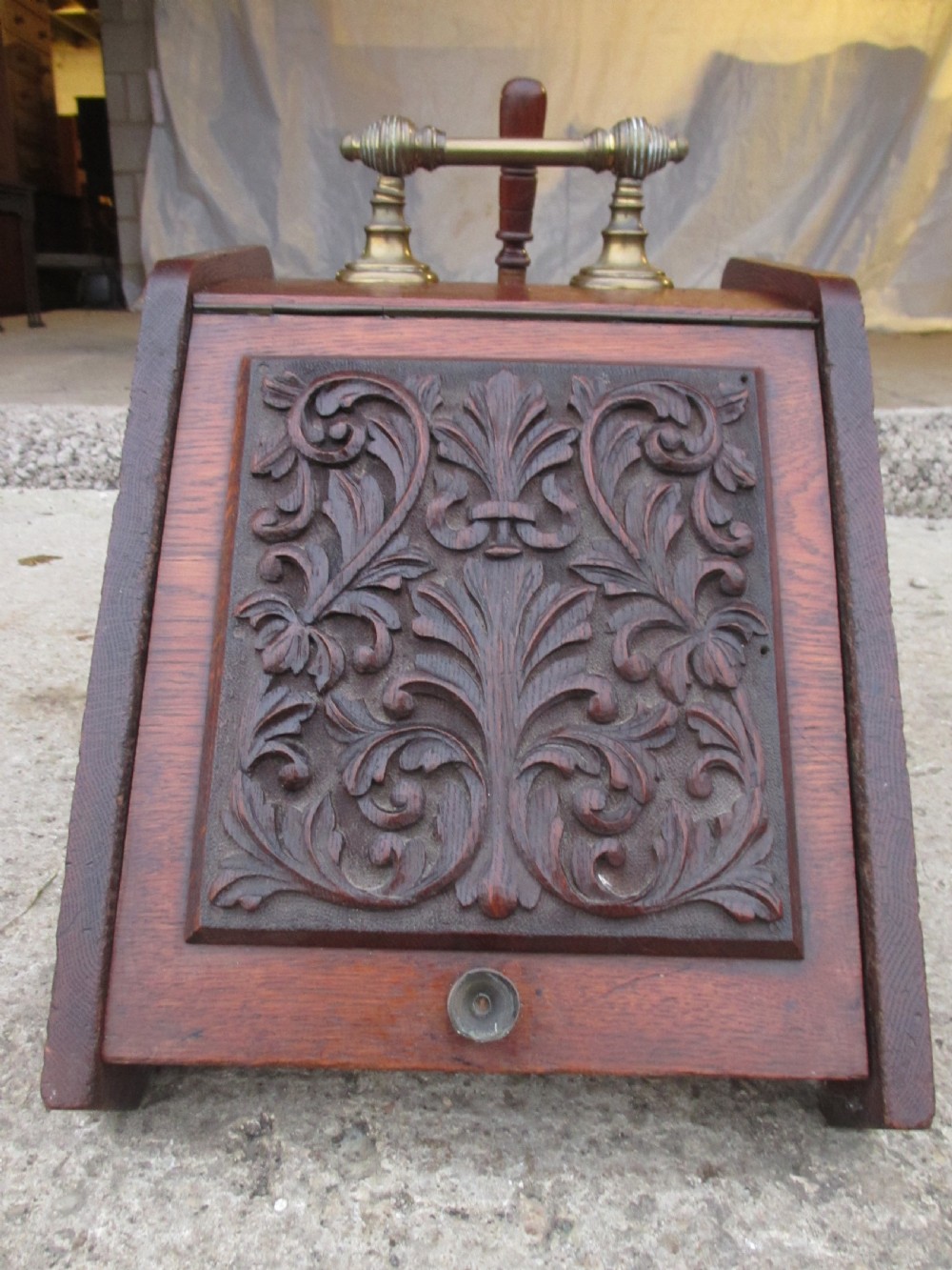 A Victorian dark oak purdonium coal box with a slanted front featuring a relief-carved acanthus leaf panel and a top brass handle. View IV