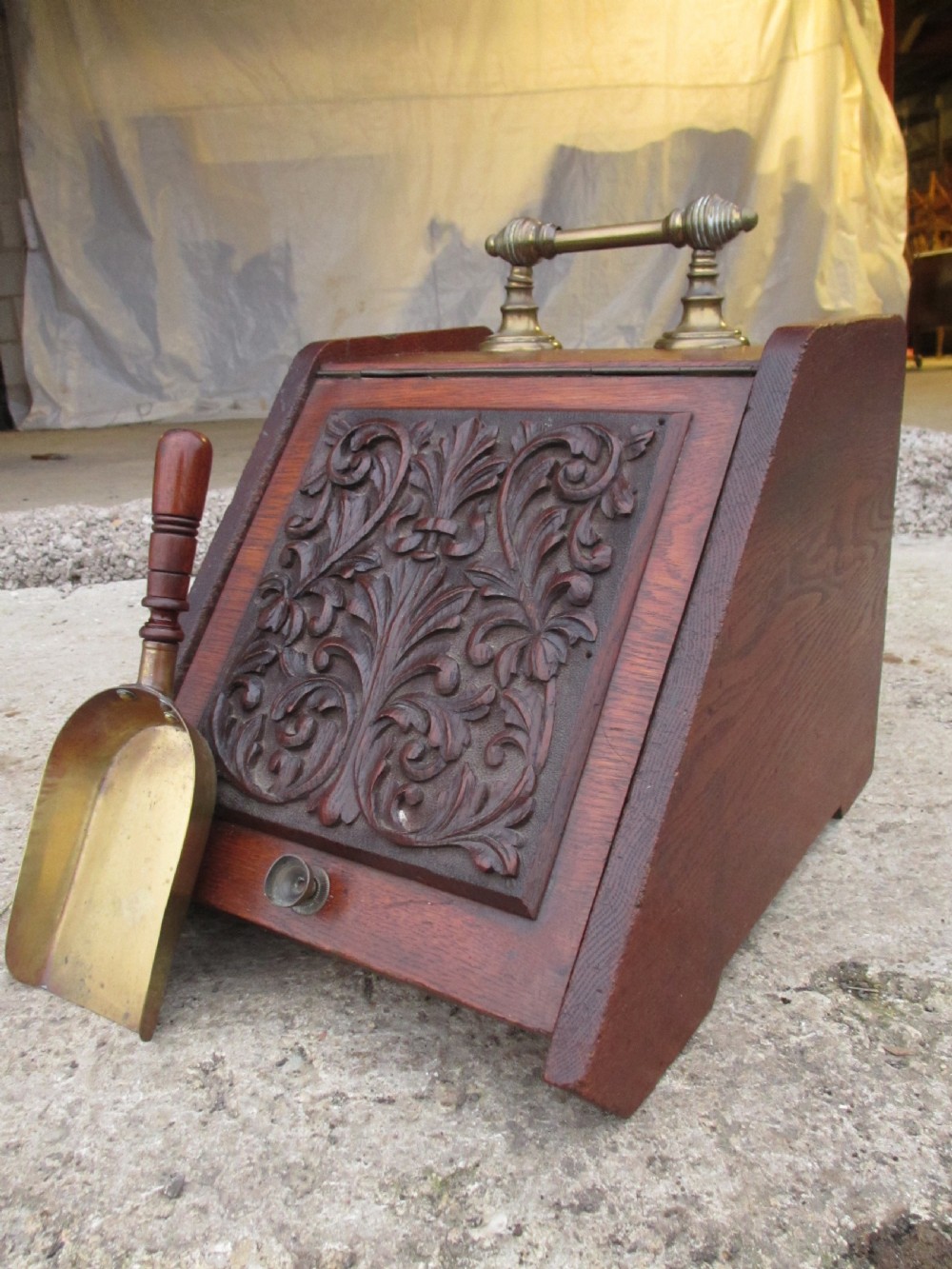 A Victorian dark oak purdonium coal box with a slanted front featuring a relief-carved acanthus leaf panel and a top brass handle. View VII