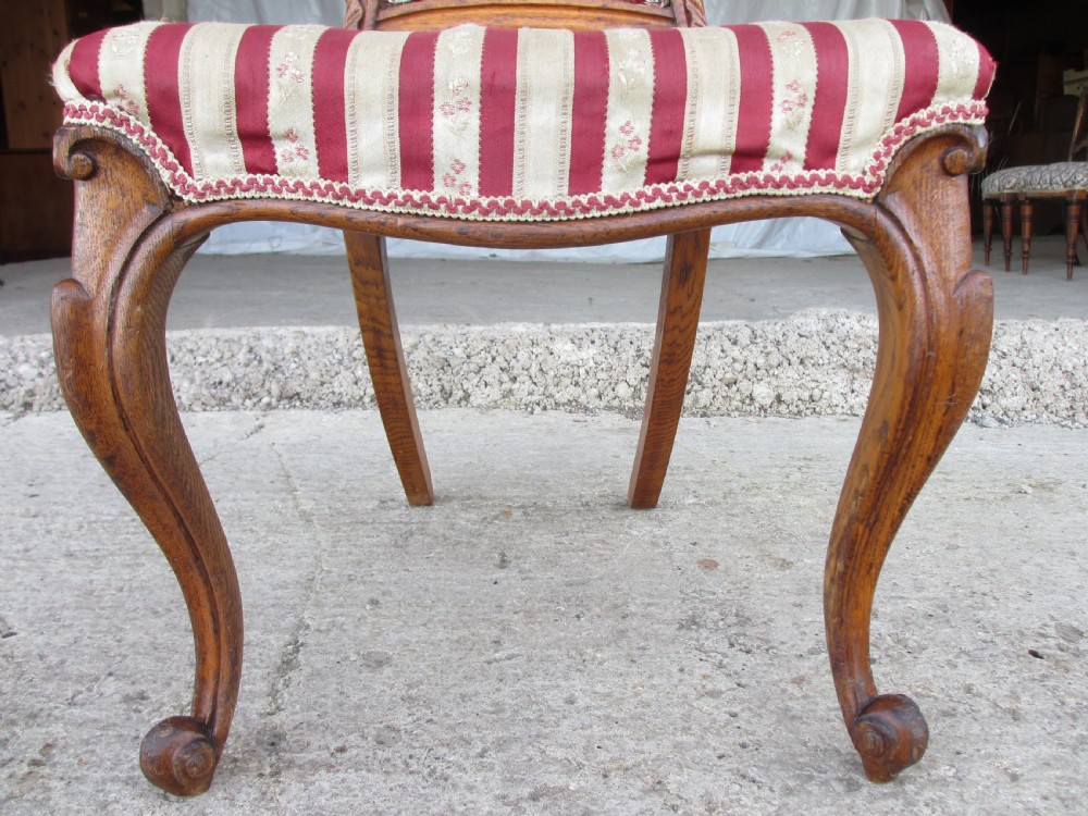 A pair of 19th-century oak balloon back dining chairs featuring red and cream striped upholstery, carved scroll details, and cabriole legs. View X