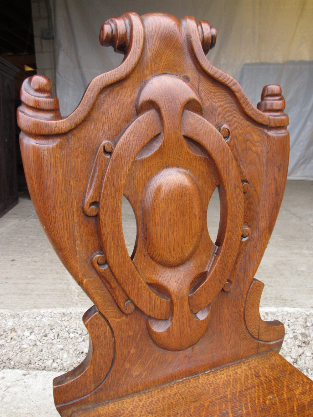 A pair of Victorian carved golden oak hall chairs featuring openwork shield backs with central cartouches, solid wooden seats, and cabriole front legs. View II
