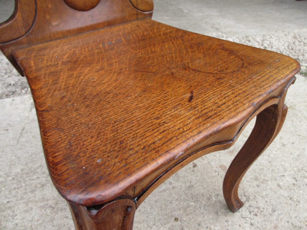 A pair of Victorian carved golden oak hall chairs featuring openwork shield backs with central cartouches, solid wooden seats, and cabriole front legs. View VI