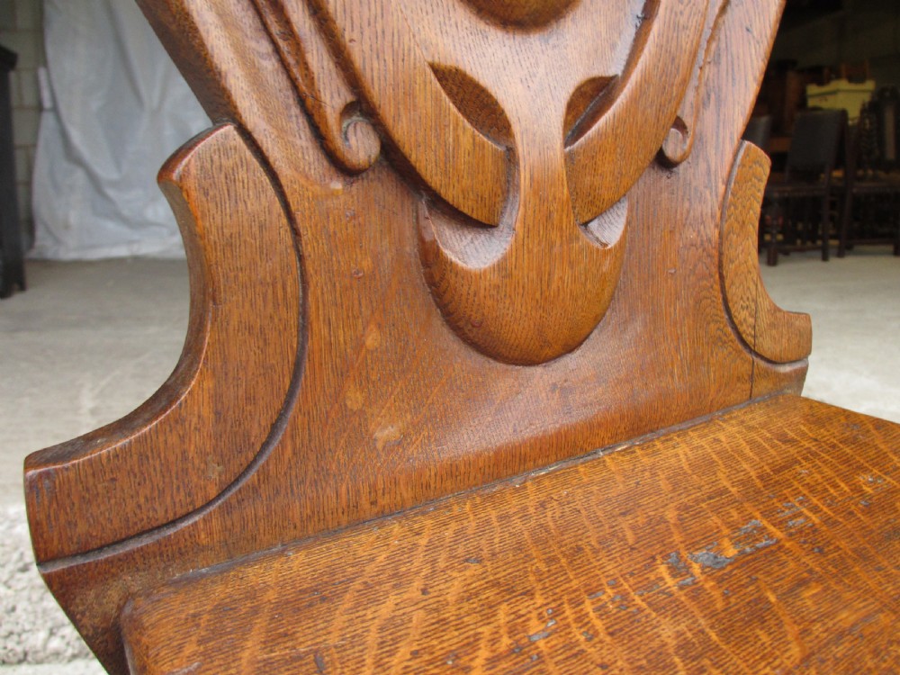 A pair of Victorian carved golden oak hall chairs featuring openwork shield backs with central cartouches, solid wooden seats, and cabriole front legs. View VII