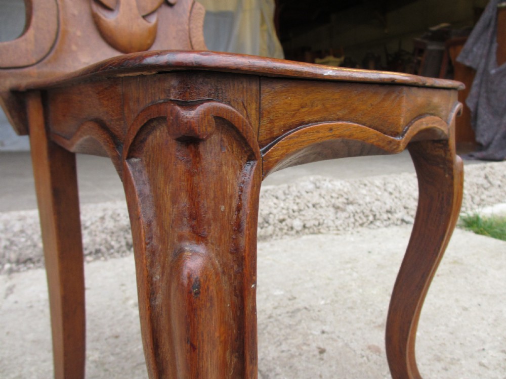 A pair of Victorian carved golden oak hall chairs featuring openwork shield backs with central cartouches, solid wooden seats, and cabriole front legs. View IX