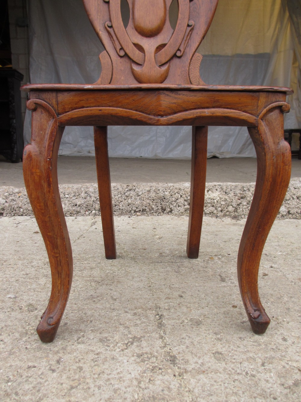 A pair of Victorian carved golden oak hall chairs featuring openwork shield backs with central cartouches, solid wooden seats, and cabriole front legs. View X