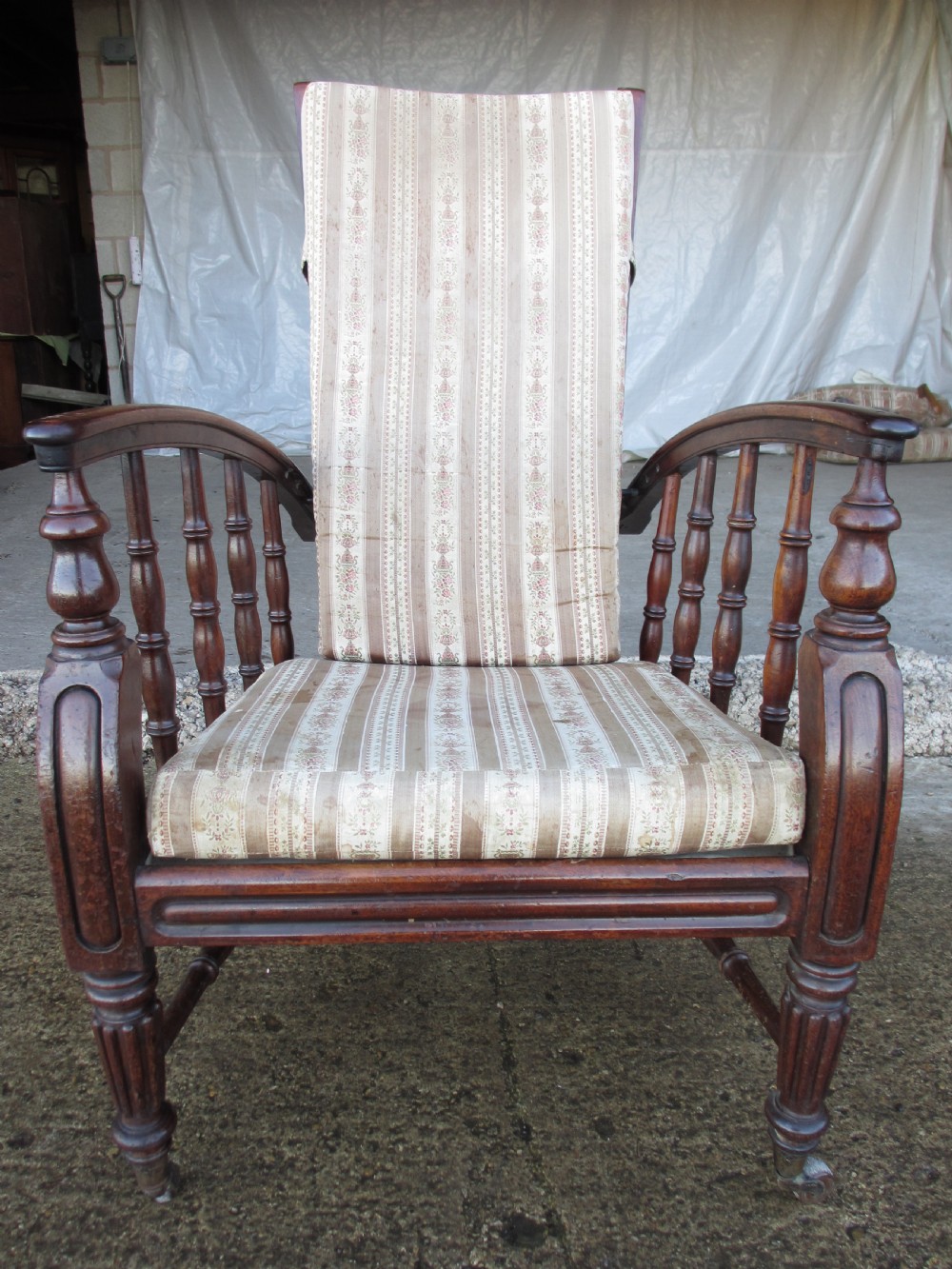 A 19th-century dark mahogany armchair featuring turned side spindles, beige striped upholstery, an adjustable reclining backrest, and brass castors. View II