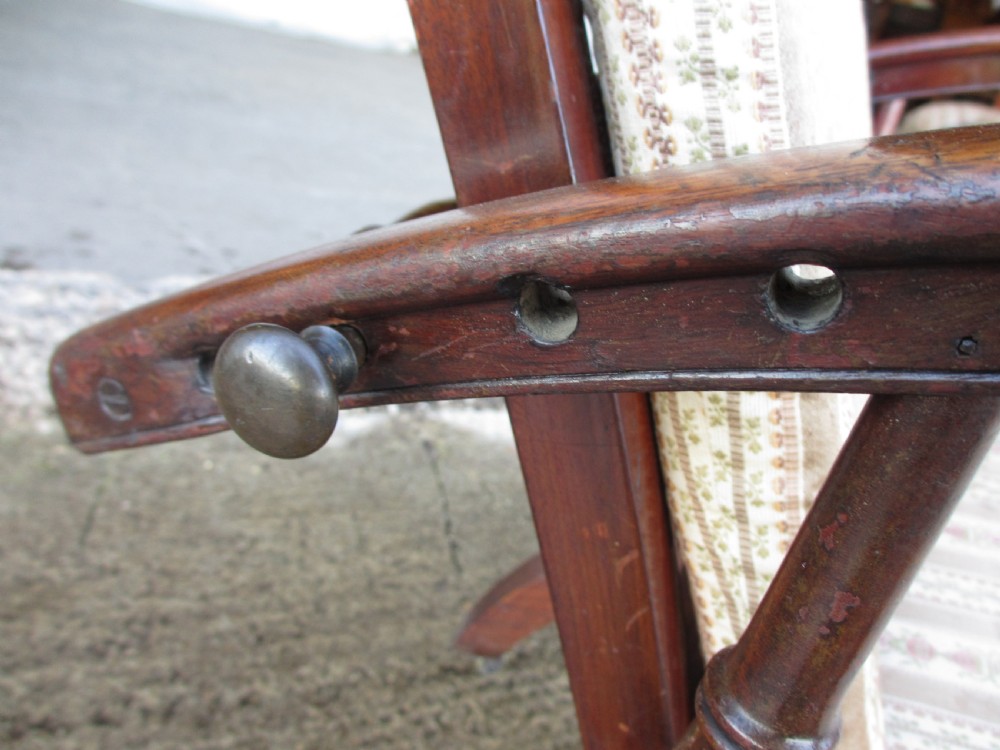 A 19th-century dark mahogany armchair featuring turned side spindles, beige striped upholstery, an adjustable reclining backrest, and brass castors. View VII