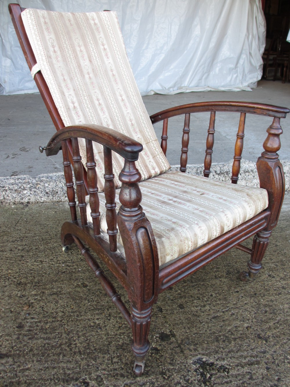 A 19th-century dark mahogany armchair featuring turned side spindles, beige striped upholstery, an adjustable reclining backrest, and brass castors. View IX